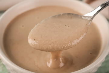 Spoon and bowl with tasty tahini, closeup
