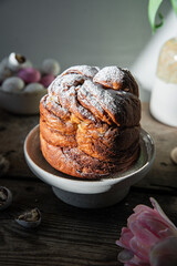 Homemade Easter bread (cruffin), chocolate eggs and pink tulips on old wooden table.
