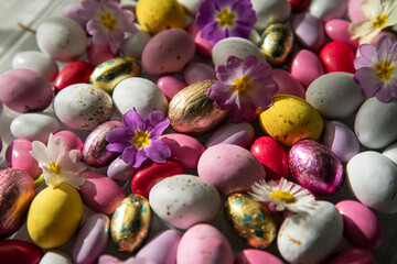 Obraz na płótnie Canvas Mix of white, pink, yellow chocolate and foiled eggs and spring flowers.