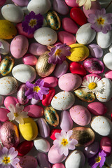 Fototapeta na wymiar Mix of white, pink, yellow chocolate and foiled eggs and spring flowers.