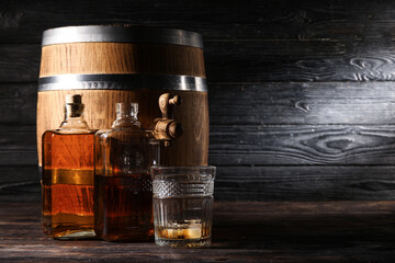 Oak barrel with bottles and glass of cold whiskey on dark wooden background