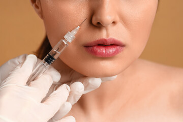 Young woman receiving filler injection in face against beige background, closeup