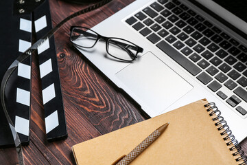 Laptop with eyeglasses, movie clapper and notebook on dark wooden background, closeup
