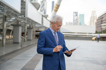 Asian senior mature middle aged businessman using tablet in modern city