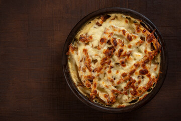 Mushroom and meat casserole covered with melted cheese and served in a dark dish on the table