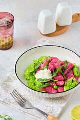 Beetroot dumplings or gnocchi with mashed green peas and curd cheese in a white plate on a light concrete background. Vegetarian recipes, beets.