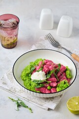 Beetroot dumplings or gnocchi with mashed green peas and curd cheese in a white plate on a light concrete background. Vegetarian recipes, beets.