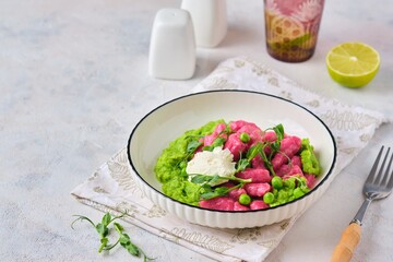 Beetroot dumplings or gnocchi with mashed green peas and curd cheese in a white plate on a light concrete background. Vegetarian recipes, beets.