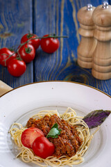 Tasty spaghetti with minced meat and cherry tomatoes on blue wooden background.