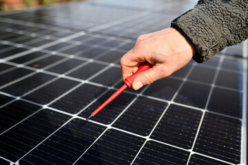 Hand vom Dachdecker Meister zeigt mit rotem Elektro Schraubenzieher Werkzeug auf Photovoltaik Dach.