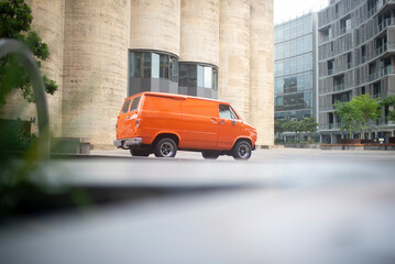 Orange 70’s boogie van rear 3/4 view landscape, with tall concrete backdrop