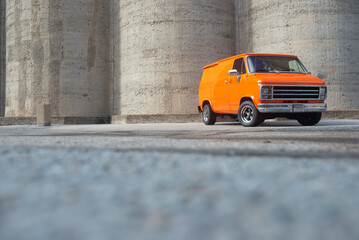 Orange 70’s boogie van front 3/4 view landscape, with concrete background