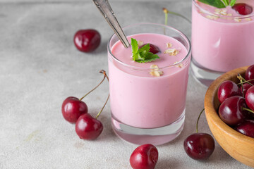 Cherry berry yogurt in glasses with fresh berries, mint and oats for healthy breakfast on gray background