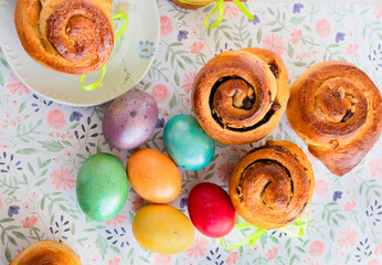  Colorful Easter eggs and sweet buns on a patterned surface. Photo from above.