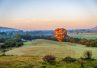 Obraz premium Hot air balloon flying over a grass field during sunrise in Magaliesburg, Gauteng, South Africa