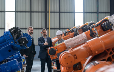 Two businessman visits robot factory. Female engineer explaining assembling robot arms welding...