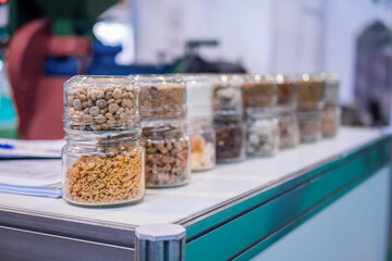 Different kinds of pelleted compound feed, fodder in glass jars: before and after extrusion - food for domestic animals at agricultural exhibition, trade show: close up. Agriculture, husbandry concept