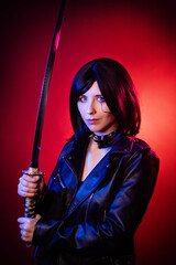 Portrait of a young woman with a bob hairstyle in a black leather jacket with a katana in her hands...