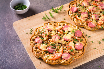 Appetizing pizza waffle with vegetables, sausages and cheese on a board on the table.