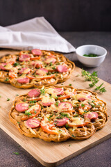 Waffle pizza with tomatoes, sausages, cheese and herbs on a wooden board. Vertical view