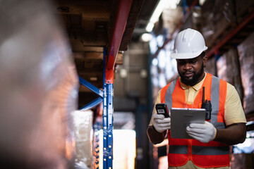 African American male warehouse worker scanning package with barcode scanner to count inventory balance in online system, holding tablet in hand for checking real time update in storage warehouse.