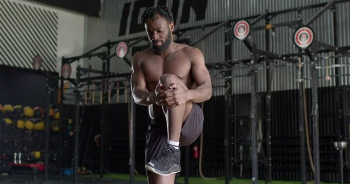 black man warming up before jogging indoors. Runner stretching muscles leg and feet and preparing to run. bearded sportsman raises,hugs legs at gym