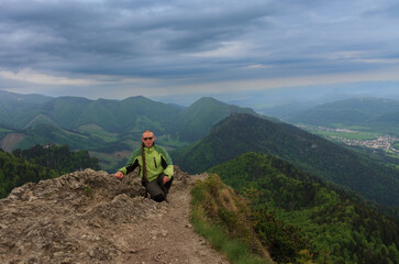 Fototapeta premium Hiker with dreadllocks on Maly Rozsutec, on background mountain village, Mala Fatra, Slovakia in spring cloudy morning