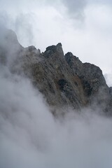 Vertical low angle shot of foggy clouds floating over rocky mountains