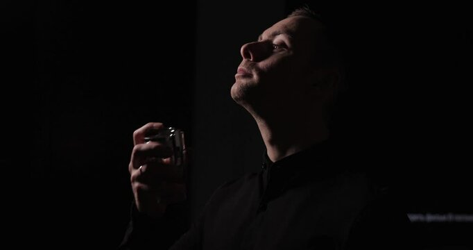 Man spraying perfume on his neck, slow motion, black dark background