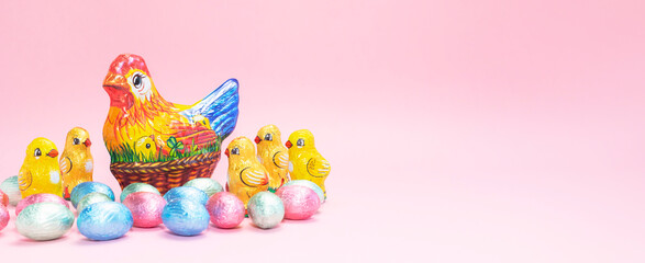 Banner Chocolate chicken, hen with colorful bright sweet eggs wrapped in foil on festive Easter...