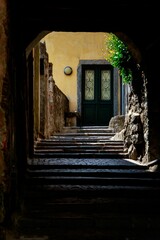 Vertical shot of a narrow walkway tunnel with stairs leading to a door in Argegno Italy