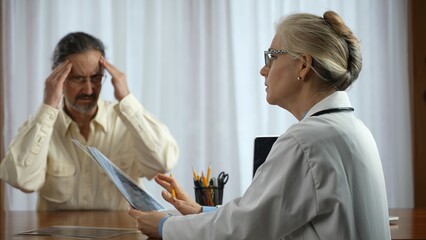 Fototapeta premium Woman doctor discuss healthcare issues with mature male patient sitting across table. Concept of doctor patient relationship in office.