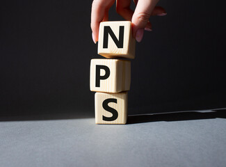 NPS - Net Promoter Score symbol. Wooden cubes with words NPS. Businessman hand. Beautiful grey background. Business and NPS concept. Copy space.