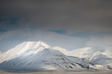 2022-05-09 SNOW COVERED MOUNTAIN PEAKS WITH A DARKENING SKY NEAR SVALBARD NORWAY IN THE ARCTIC
