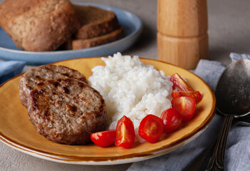 cutlets, rice, cherry tomatoes on a yellow plate, close-up