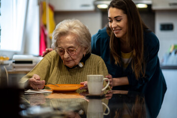 Senior woman eating her soup while her caretaker is proudly smiling.
