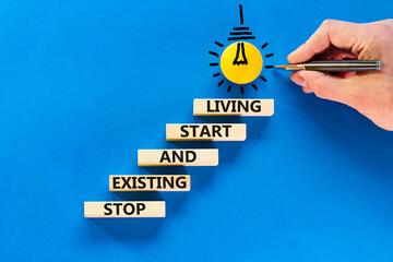 Stop existing start living symbol. Concept words Stop existing and start living on wooden blocks. Beautiful blue background. Businessman hand. Business Stop existing start living concept. Copy space.