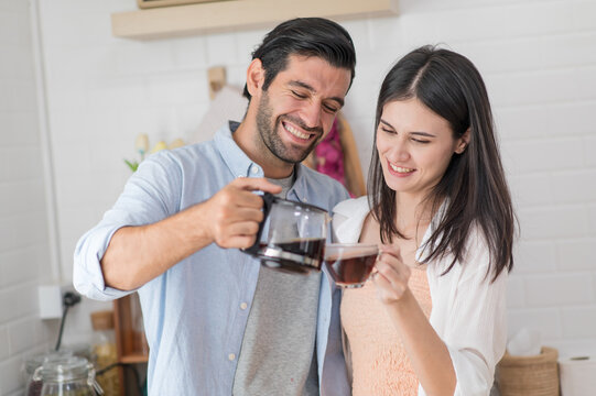 Happy couple in love cooking in the kitchen at home, man making coffee for his girlfriend
