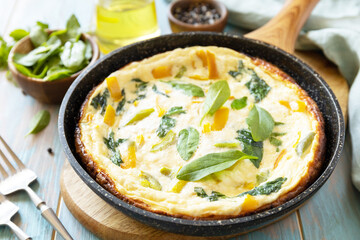 Healthy frittata or stuffed omelette in pan on rustic wooden background. Italian omelette with organic spinach and bell pepper.