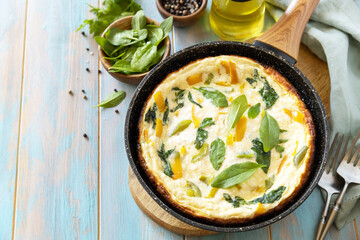 Healthy frittata or stuffed omelette in pan on rustic wooden background. Italian omelette with organic spinach and bell pepper. Copy space.