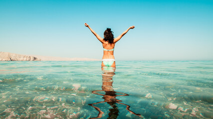Young carefree caucasian woman stand excited hands spread in turquoise water beach alone on summer...