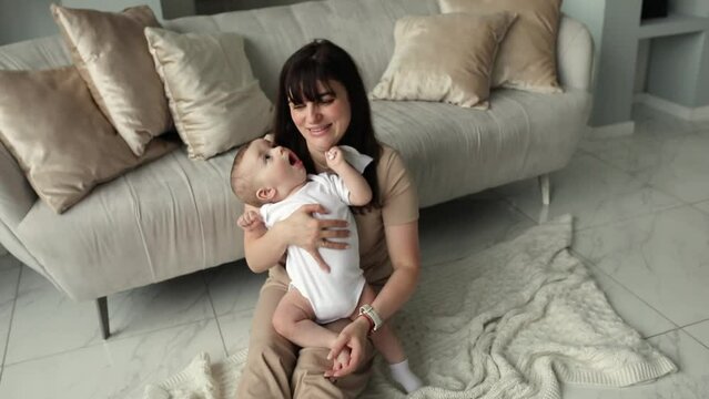 Full body photo of pretty positive woman and adorable toddler sitting on the floor, rest,relax spend free time indoors
