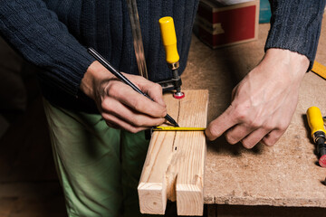 A carpenter works in a furniture workshop with various tools and a board