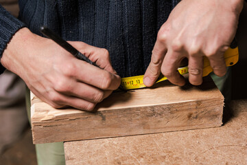 A carpenter works in a furniture workshop with various tools and a board