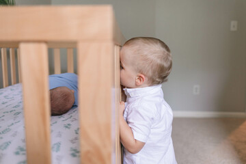 Big brother looking through crib at newborn