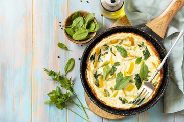 Healthy frittata or stuffed omelette in pan on rustic wooden background. Italian omelette with organic spinach and bell pepper. View from above. Copy space.