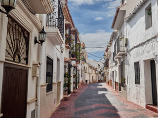 Nerja, Spain - October 9, 2021: Typical Andalusian street with whitewashed houses in a sunny day.  Nerja, beautiful touristic village in Costa del Sol. Malaga province, Andausia, Spain, Europe - obrazy, fototapety, plakaty