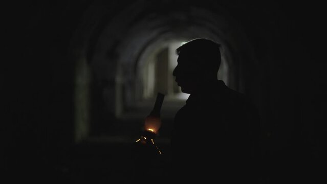 A man in a dungeon with a gas lamp and then blows it out. The boy extinguishes the lamp, sparks fly, darkness sets in. A mystical scene in the catacombs. High quality 4k footage