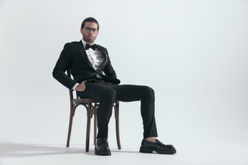 elegant attractive man with glasses sitting with hands in pockets