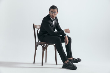 side view of shocked elegant man in black tuxedo sitting with elbows on thighs